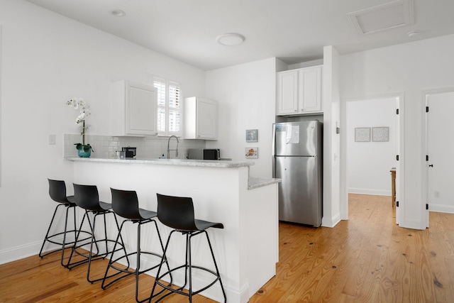 kitchen featuring light wood-style floors, freestanding refrigerator, white cabinets, and a peninsula