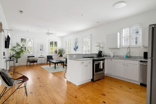 kitchen with stainless steel appliances, white cabinetry, a sink, light wood-type flooring, and a peninsula