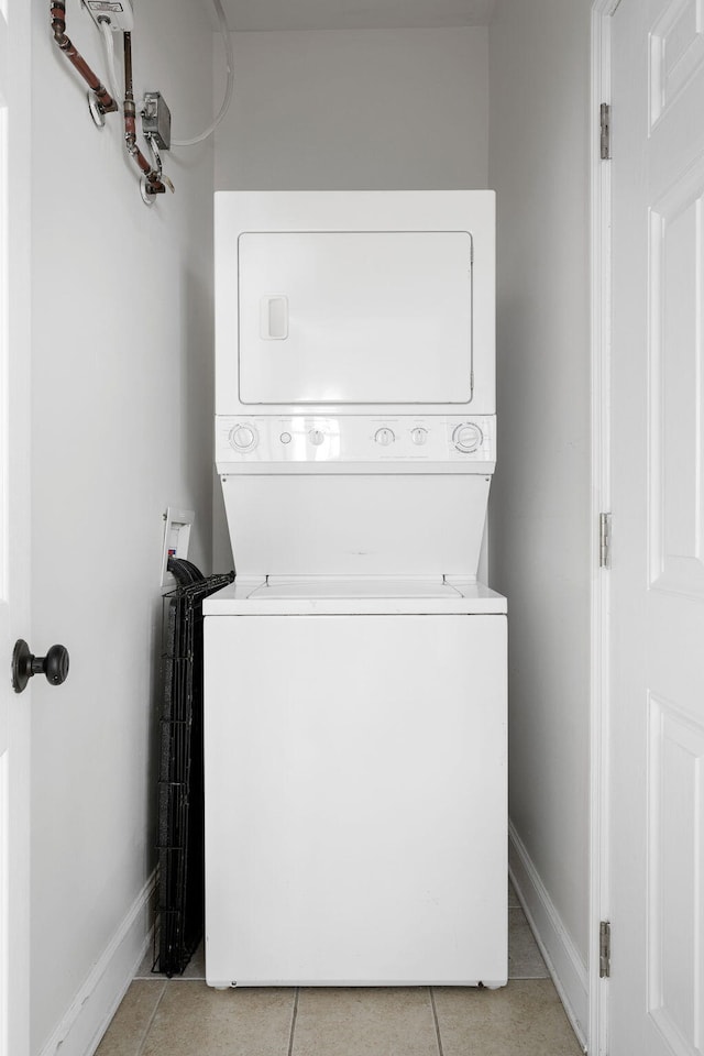 clothes washing area featuring stacked washer / drying machine, laundry area, light tile patterned flooring, and baseboards