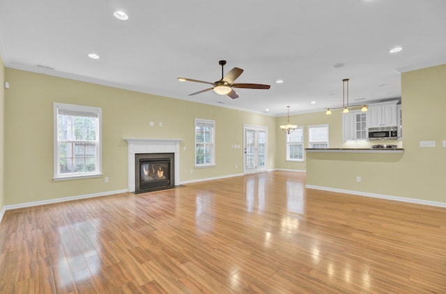 unfurnished living room featuring crown molding, a healthy amount of sunlight, ceiling fan with notable chandelier, and light hardwood / wood-style flooring