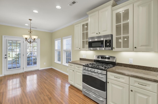 kitchen featuring white cabinetry, appliances with stainless steel finishes, dark stone counters, ornamental molding, and pendant lighting