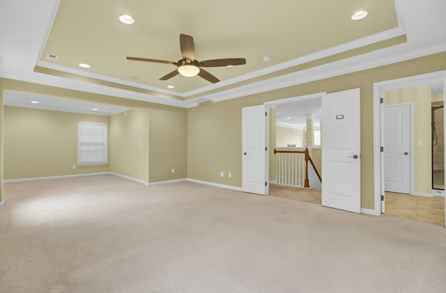 unfurnished room with a raised ceiling, light carpet, ornamental molding, and ceiling fan