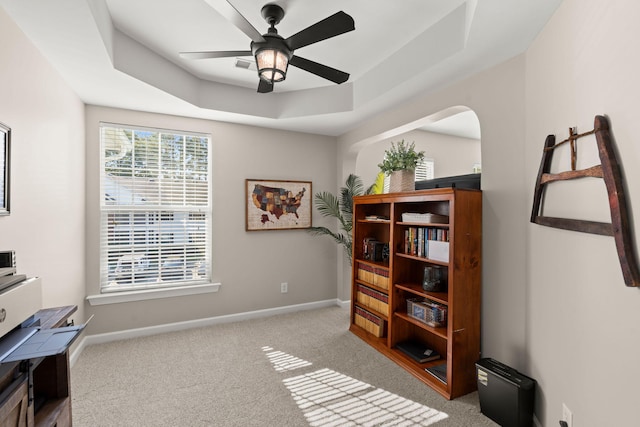 interior space with ceiling fan, a tray ceiling, and light colored carpet