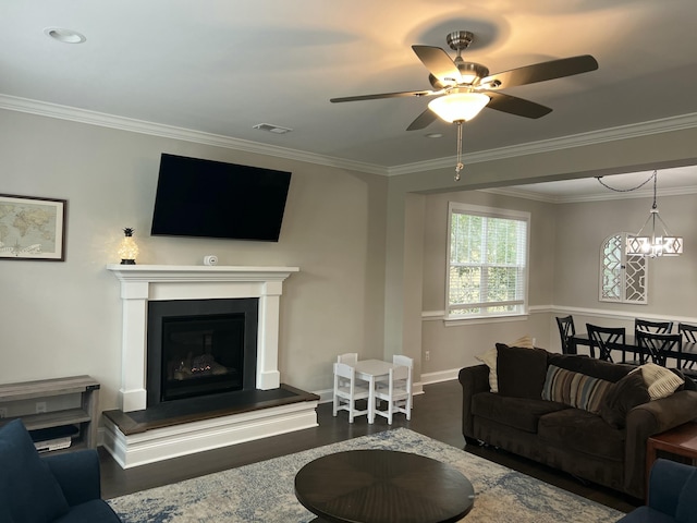 living area with crown molding, visible vents, a glass covered fireplace, wood finished floors, and ceiling fan with notable chandelier