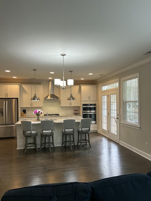 kitchen with dark wood-style floors, wall chimney exhaust hood, light countertops, appliances with stainless steel finishes, and a kitchen bar