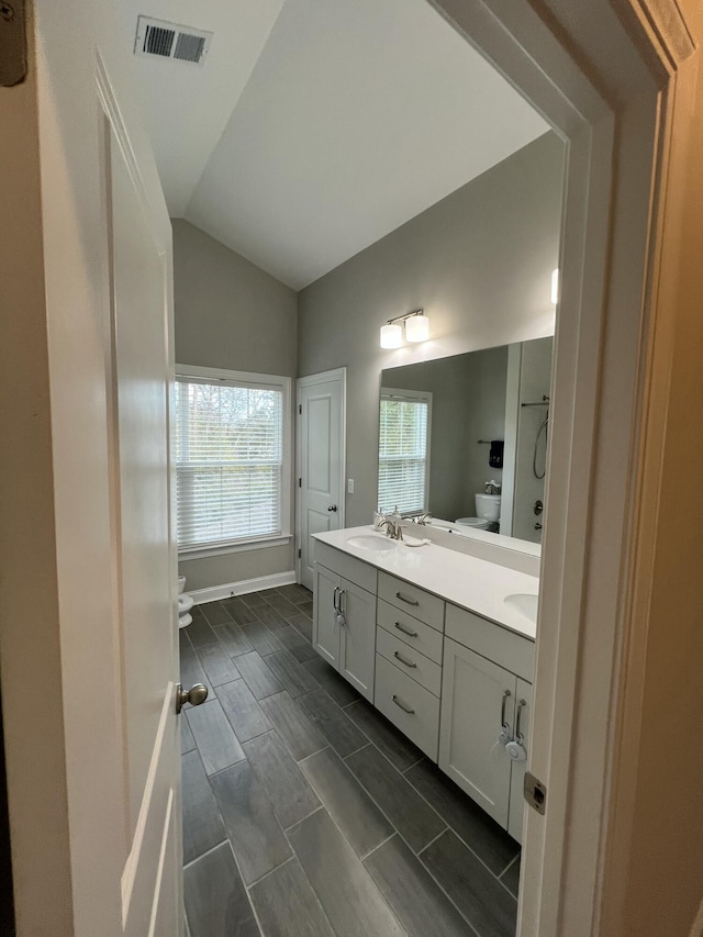 full bathroom with double vanity, visible vents, toilet, lofted ceiling, and a sink