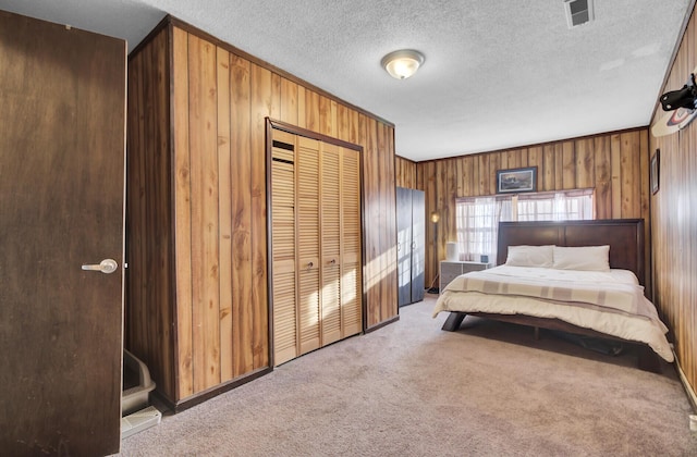 bedroom featuring a textured ceiling, light carpet, wooden walls, and a closet