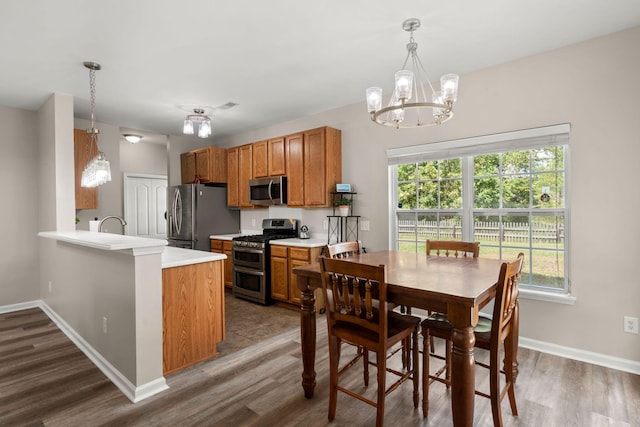 kitchen with kitchen peninsula, stainless steel appliances, an inviting chandelier, dark hardwood / wood-style floors, and hanging light fixtures