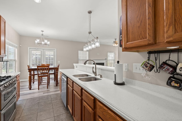 kitchen with sink, stainless steel appliances, pendant lighting, light tile patterned floors, and ceiling fan with notable chandelier