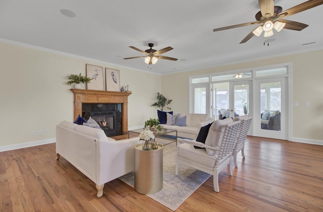 living room with a tiled fireplace, ornamental molding, french doors, and light wood-type flooring