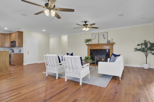 living room with crown molding, ceiling fan, a tiled fireplace, and hardwood / wood-style floors