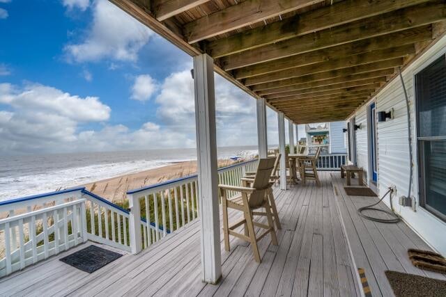 wooden terrace featuring a water view and a beach view