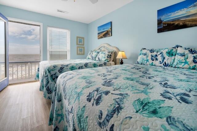 bedroom with light wood-type flooring, access to outside, a water view, and ceiling fan