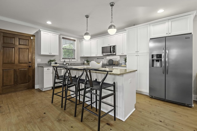 kitchen with a breakfast bar, stainless steel appliances, light wood-style floors, pendant lighting, and white cabinetry