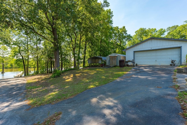 view of front facade with aphalt driveway, a carport, a water view, an outbuilding, and a detached garage
