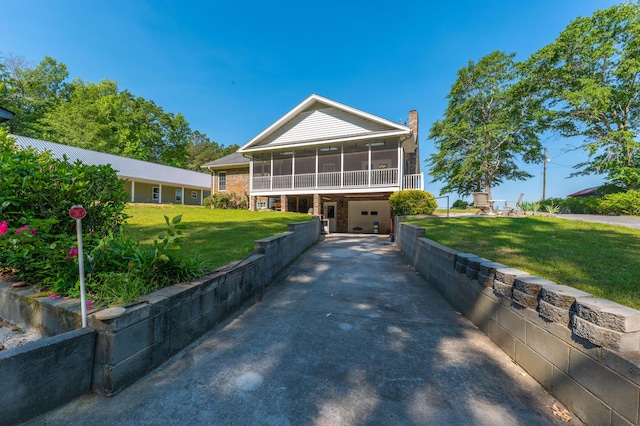 view of front of home with a chimney, a front yard, a sunroom, a garage, and concrete driveway