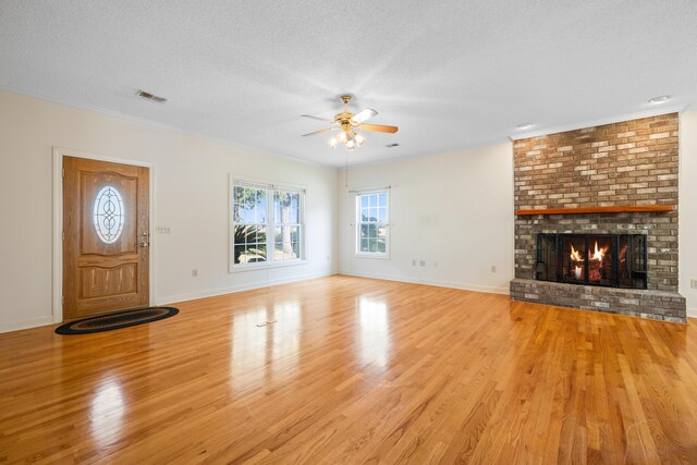 unfurnished living room featuring ceiling fan, a brick fireplace, a textured ceiling, wood finished floors, and visible vents