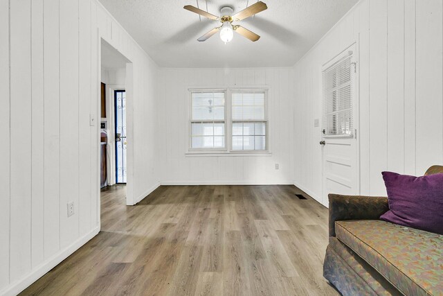 interior space with ceiling fan, wooden walls, light hardwood / wood-style flooring, and a textured ceiling