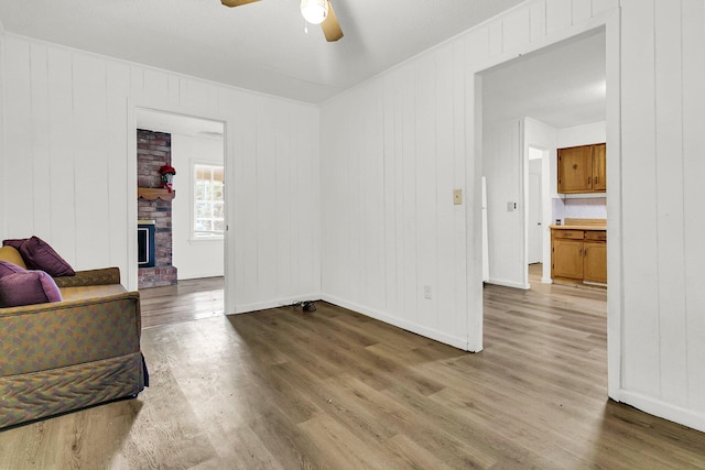 living room with hardwood / wood-style floors, wood walls, a brick fireplace, and ceiling fan