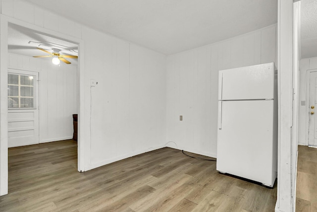 empty room featuring ceiling fan, wooden walls, and light hardwood / wood-style floors