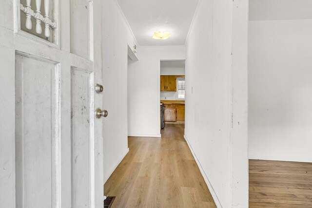 corridor featuring ornamental molding, light hardwood / wood-style floors, and a textured ceiling