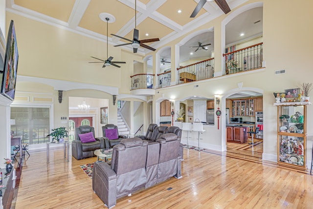 living room with ceiling fan with notable chandelier, a towering ceiling, and light hardwood / wood-style floors