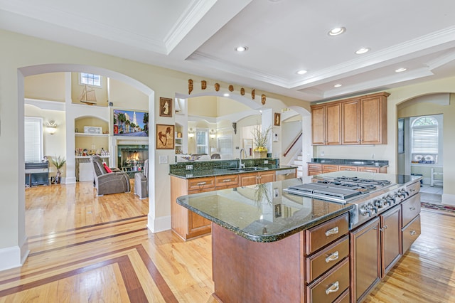 kitchen with a center island with sink, light hardwood / wood-style floors, stainless steel gas cooktop, and dark stone countertops