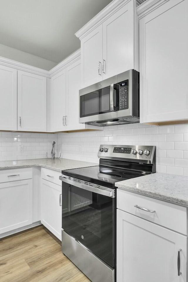 kitchen featuring appliances with stainless steel finishes, white cabinetry, tasteful backsplash, light stone countertops, and light wood-type flooring