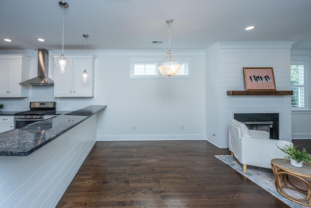 kitchen with wall chimney range hood, stainless steel gas stove, white cabinets, recessed lighting, and dark stone counters
