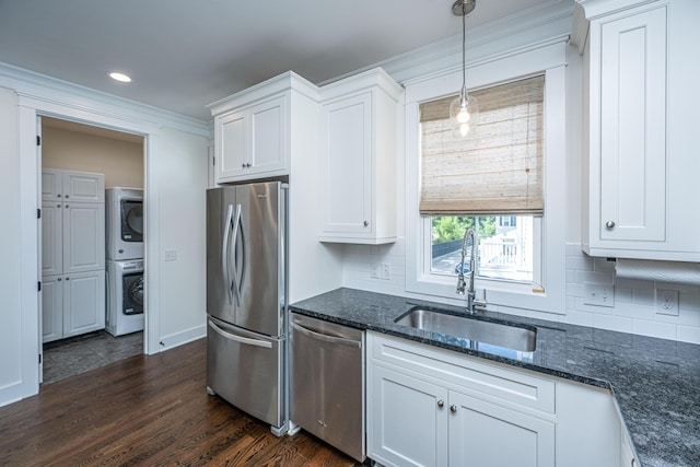 kitchen featuring appliances with stainless steel finishes, estacked washer and dryer, a sink, white cabinets, and dark stone countertops