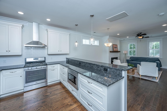 kitchen with stainless steel appliances, wall chimney exhaust hood, a peninsula, white cabinetry, and recessed lighting