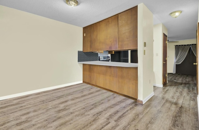 kitchen with light hardwood / wood-style floors, a textured ceiling, black fridge, decorative backsplash, and kitchen peninsula