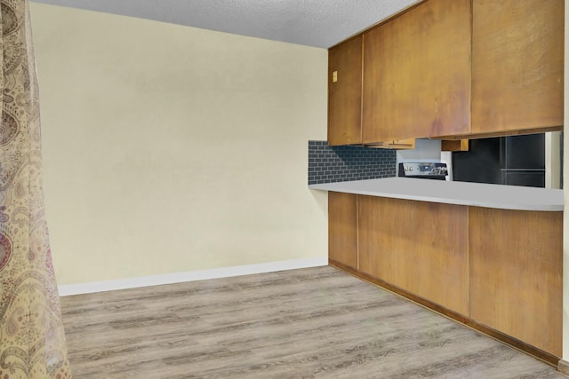 kitchen featuring black fridge, tasteful backsplash, light hardwood / wood-style flooring, a textured ceiling, and electric stove