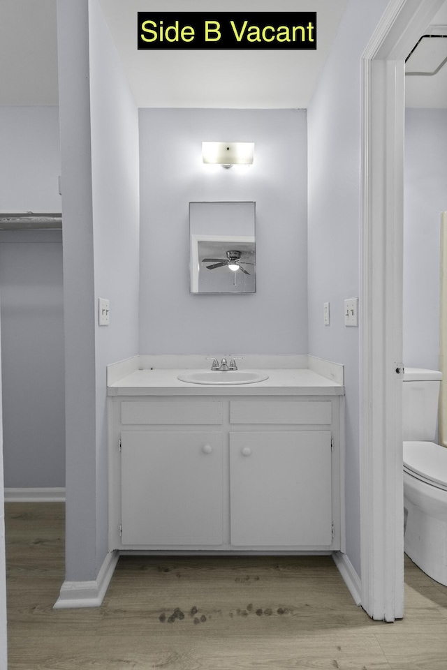 bathroom featuring baseboards, toilet, wood finished floors, and vanity