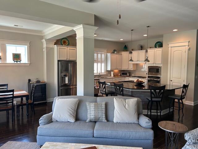 living area featuring ornate columns, baseboards, ornamental molding, recessed lighting, and dark wood-type flooring