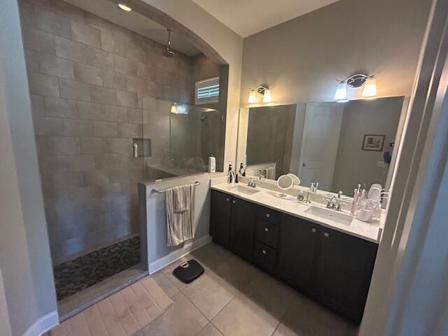 bathroom featuring baseboards, double vanity, tiled shower, a sink, and tile patterned flooring