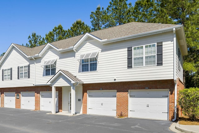 townhome / multi-family property featuring a garage, brick siding, and a shingled roof