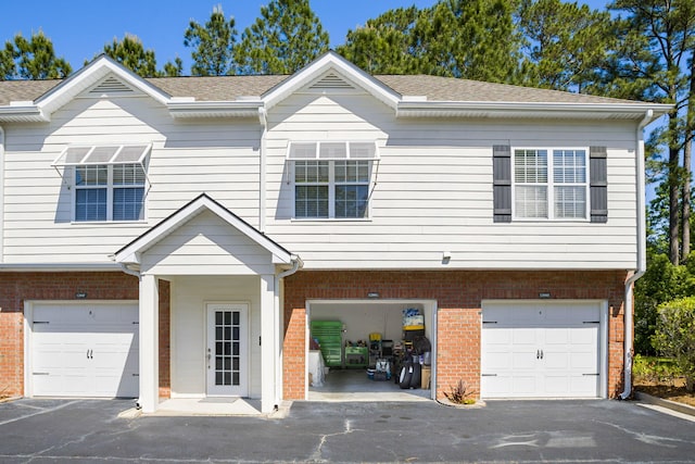 townhome / multi-family property featuring driveway, roof with shingles, and brick siding