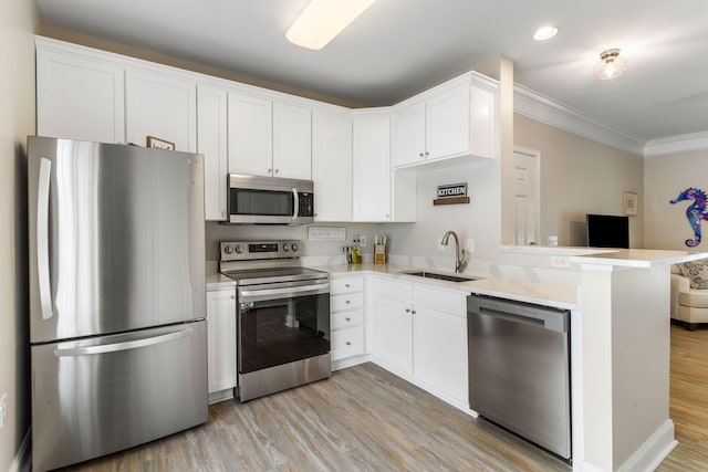 kitchen featuring light wood finished floors, crown molding, appliances with stainless steel finishes, and a sink