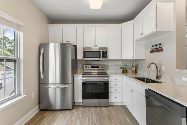 kitchen with appliances with stainless steel finishes, a sink, light wood-style flooring, and white cabinets