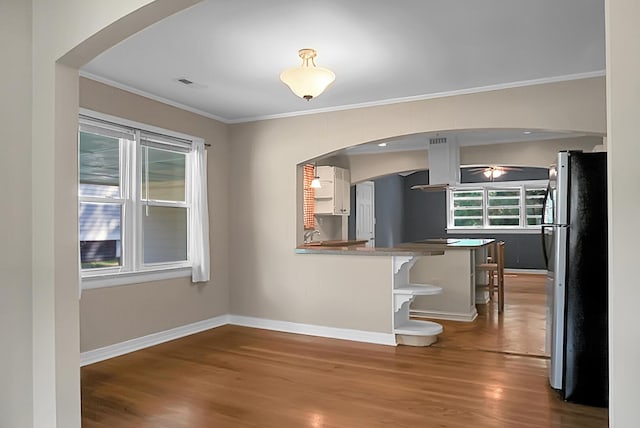 kitchen with a breakfast bar area, stainless steel fridge, hardwood / wood-style flooring, kitchen peninsula, and crown molding