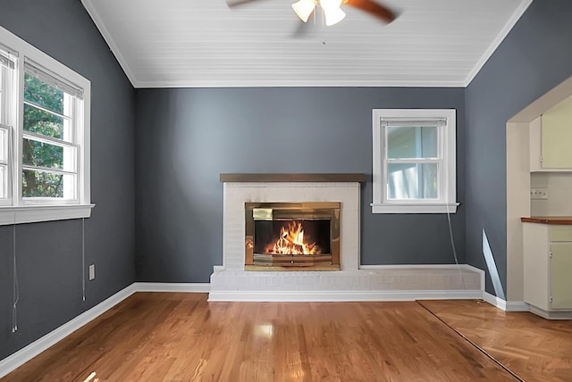 unfurnished living room featuring crown molding, a brick fireplace, ceiling fan, and light wood-type flooring