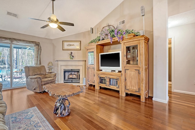 living area with a warm lit fireplace, visible vents, vaulted ceiling, and wood finished floors