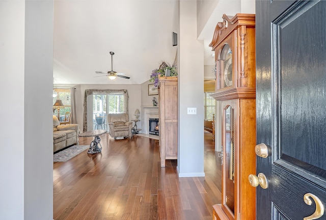 entryway featuring a ceiling fan, a lit fireplace, a towering ceiling, and wood finished floors