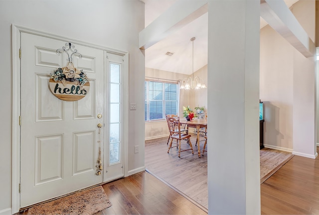 entrance foyer with lofted ceiling, visible vents, an inviting chandelier, wood finished floors, and baseboards