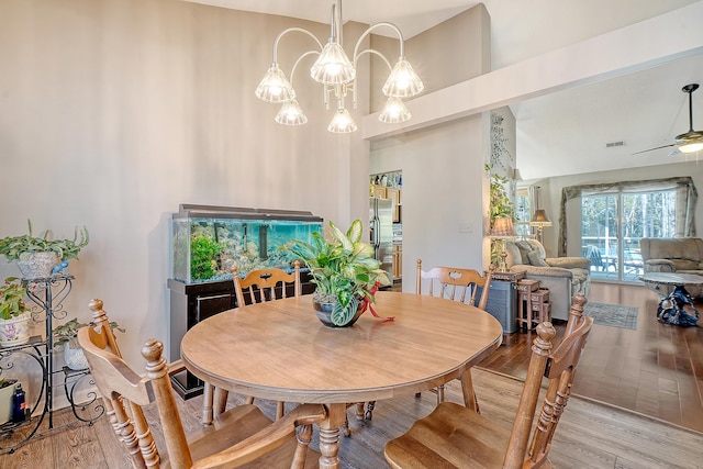 dining area with visible vents, vaulted ceiling, wood finished floors, and ceiling fan with notable chandelier