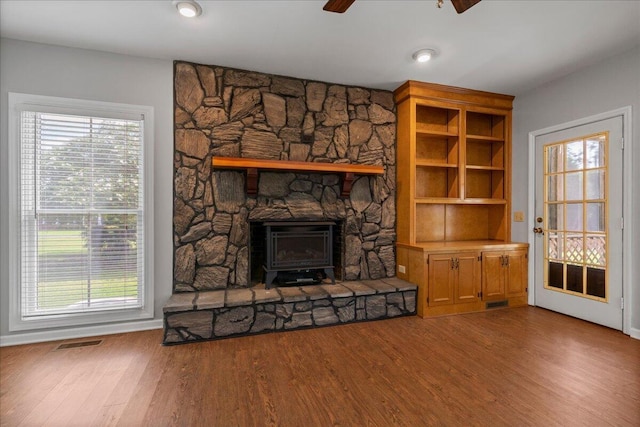 unfurnished living room with wood-type flooring, a wood stove, and ceiling fan