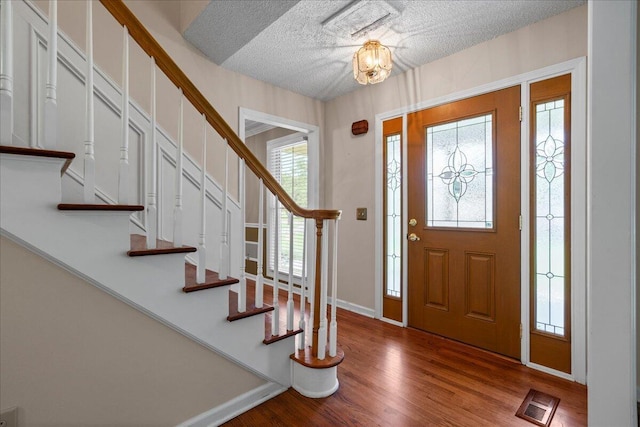 foyer entrance featuring hardwood / wood-style floors, a notable chandelier, and a textured ceiling