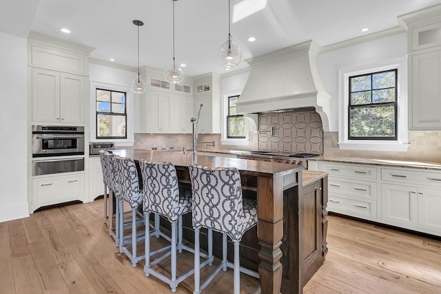 kitchen featuring custom exhaust hood, white cabinetry, a kitchen island with sink, and stainless steel oven