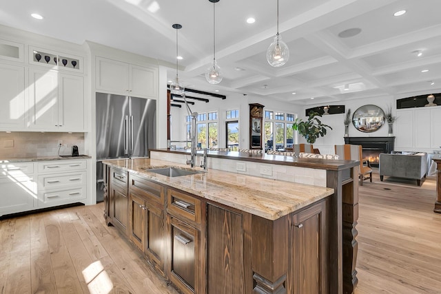 kitchen featuring white cabinets, a center island with sink, light wood-type flooring, beamed ceiling, and pendant lighting